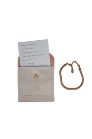An image of an open bracelet box with a card inside and a gold-plated bracelet placed beside it on a neutral background.
