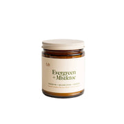 Jar of candle labeled 'Evergreen + Mistletoe' on a white background