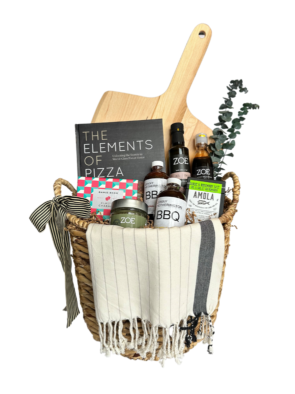 This is a picture of a Home Pizza Gift Basket. There's a personalized wooden pizza paddle, infused olive oil, balsamic glaze, gourmet bbq sauces, herb sea salt, a game of charades and "The Elements of Pizza" cookbook.
