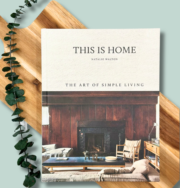 This is a picture of the book "This Is Home, The Art of Simple Living" by Natalie Walton and a beautiful wooden cutting board