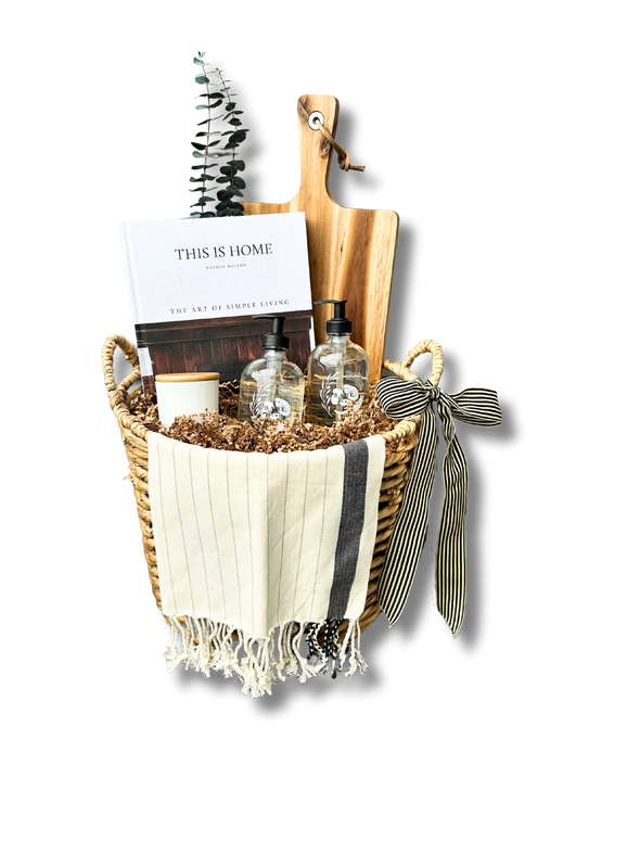 This is a picture of a gift basket for home buyers full of hand soap, dish soap, Turkish tea towel, personalized cutting board, This Is Home coffee table book and a beautifully scented candle.